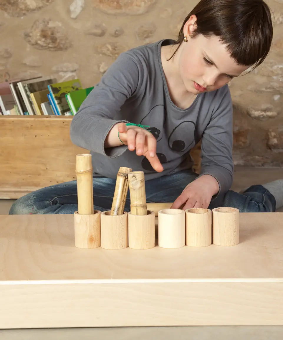 Row of Grapat handcrafted unpainted wooden cups with a bamboo sticks inside and a child in the background.