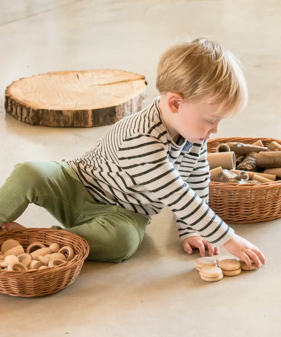 Child sorting Grapat's natural handcrafted wooden disks on a concrete floor