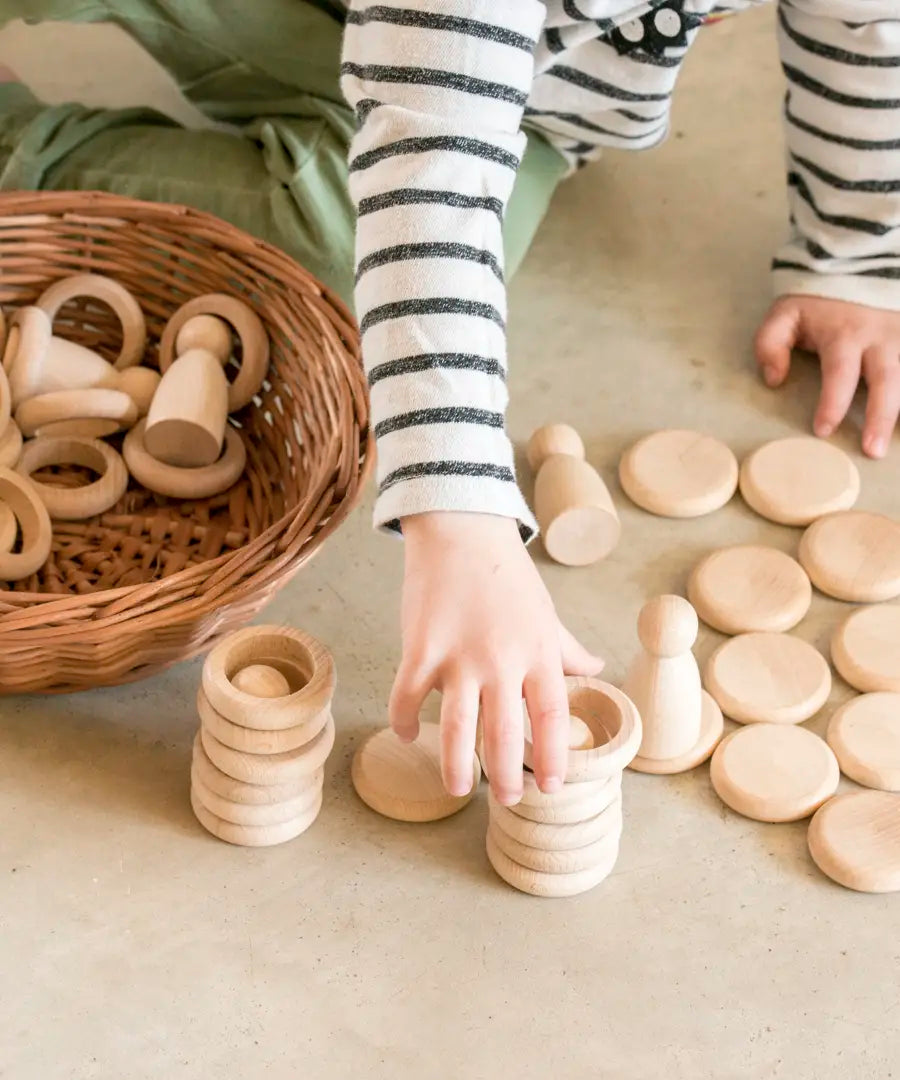 Child hands stacking Grapat handcrafted natural wooden rings and disks on a concrete surface 