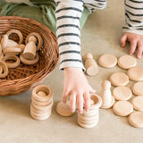 Child hands stacking Grapat handcrafted natural wooden rings and disks on a concrete surface 