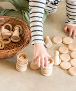 Child hands stacking Grapat handcrafted natural wooden rings and disks on a concrete surface 