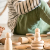 A stack of Grapat 's handcrafted wooden rings next to wooden peg dolls and coins