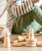 A stack of Grapat 's handcrafted wooden rings next to wooden peg dolls and coins