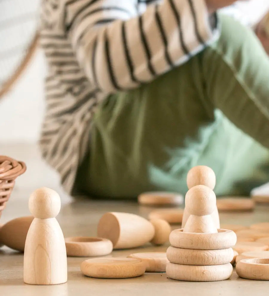 A stack of Grapat 's handcrafted wooden rings next to wooden peg dolls and coins