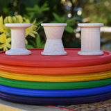 Grapat loose parts 3 natural wooden spools stacked on a stack of Grapat rainbow dishes.
