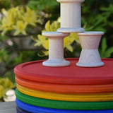 Grapat loose parts 3 natural wooden spools stacked on a stack of Grapat rainbow dishes.