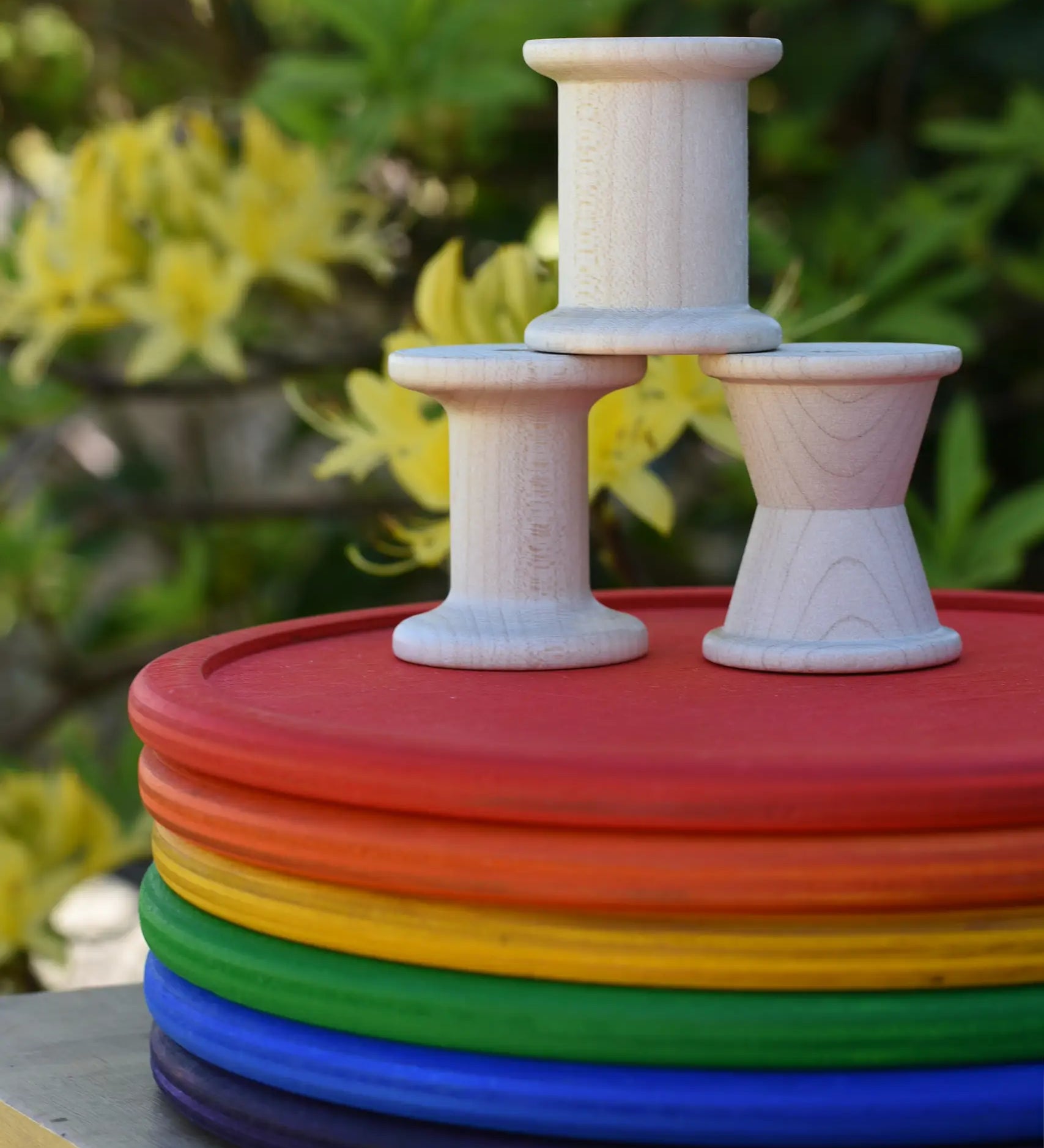 Grapat loose parts 3 natural wooden spools stacked on a stack of Grapat rainbow dishes.