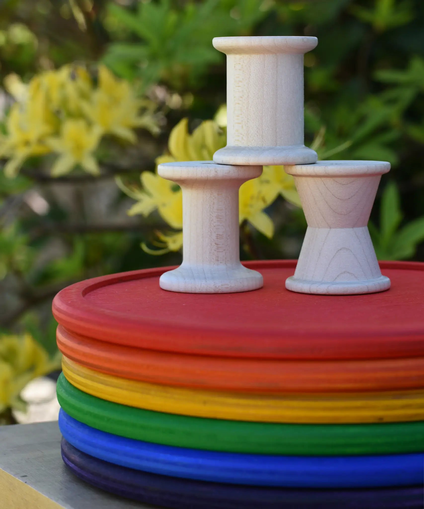 Grapat loose parts 3 natural wooden spools stacked on a stack of Grapat rainbow dishes.
