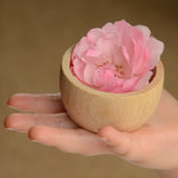 Grapat natural wooden toy bowl with a pink flower placed inside, placed on a child's hand.
