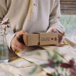 A close up of a child's hand holding the box that contains the Grapat and Ostheimer collaboration  Handmade Seasonal Play Set Hello Spring Set.