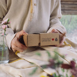 A close up of a child's hand holding the box that contains the Grapat and Ostheimer collaboration  Handmade Seasonal Play Set Hello Spring Set.