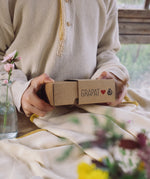A close up of a child's hand holding the box that contains the Grapat and Ostheimer collaboration  Handmade Seasonal Play Set Hello Spring Set.