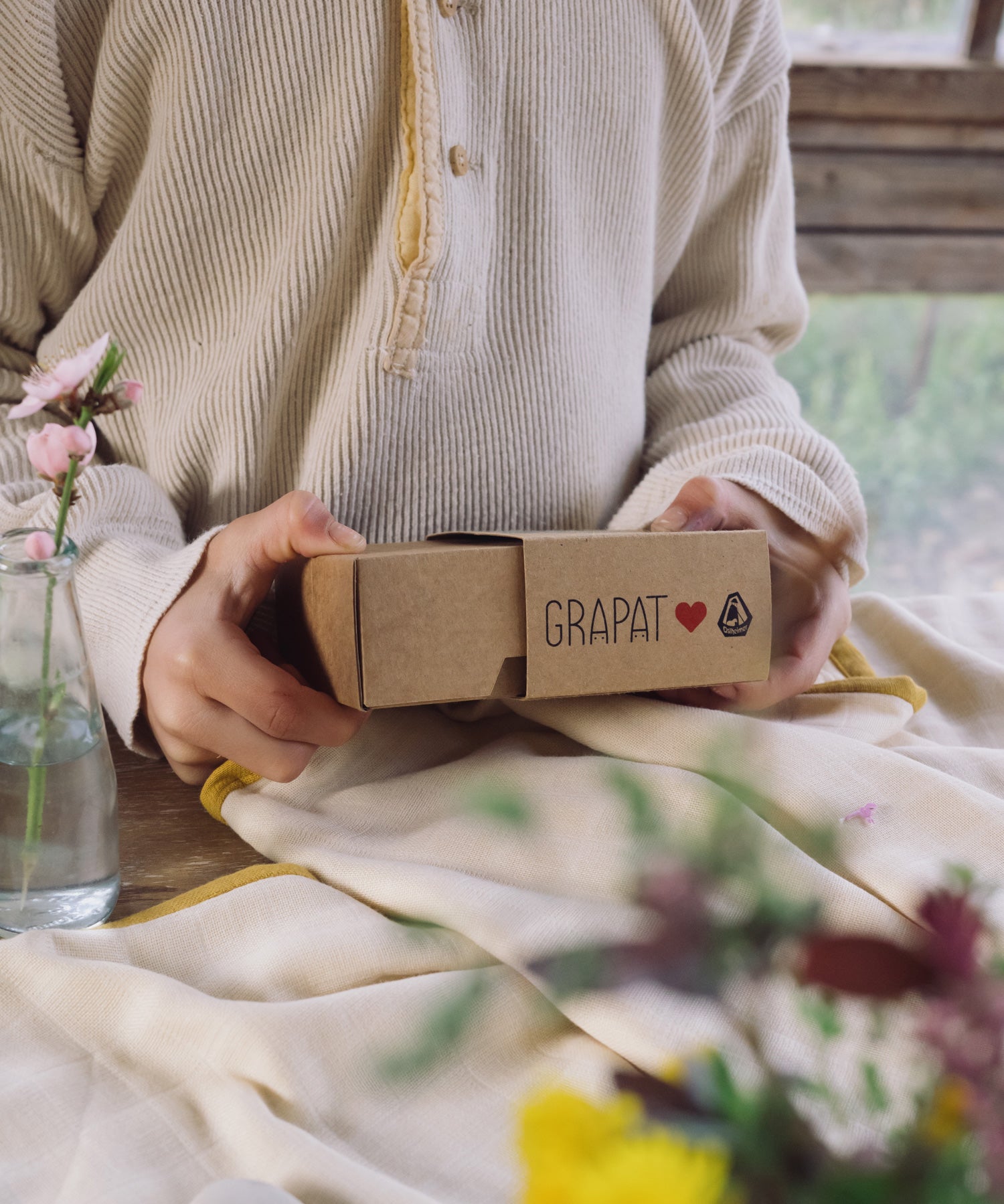 A close up of a child's hand holding the box that contains the Grapat and Ostheimer collaboration  Handmade Seasonal Play Set Hello Spring Set.