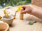 A child's hand holding the peg doll from the Grapat / Ostheimer Hello Summer set showing the hand painted detail and scale.   Standing next to the wooden goose on a table cloth 