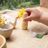 A child's hand holding the peg doll from the Grapat / Ostheimer Hello Summer set showing the hand painted detail and scale.   Standing next to the wooden goose on a table cloth 