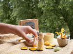 A child's hand playing outside holding the wooden goose from the Grapat / Ostheimer Hello Summer set next to the wooden peg doll figure showing the delicate hand painted detail with the small bowl and decorative box in the background.