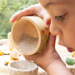 A child playing outside and holding the small wooden bowl from the Grapat / Ostheimer set showing the scale and tipping sand into a small stone bowl
