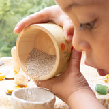 A child playing outside and holding the small wooden bowl from the Grapat / Ostheimer set showing the scale and tipping sand into a small stone bowl