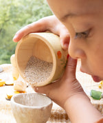 A child playing outside and holding the small wooden bowl from the Grapat / Ostheimer set showing the scale and tipping sand into a small stone bowl