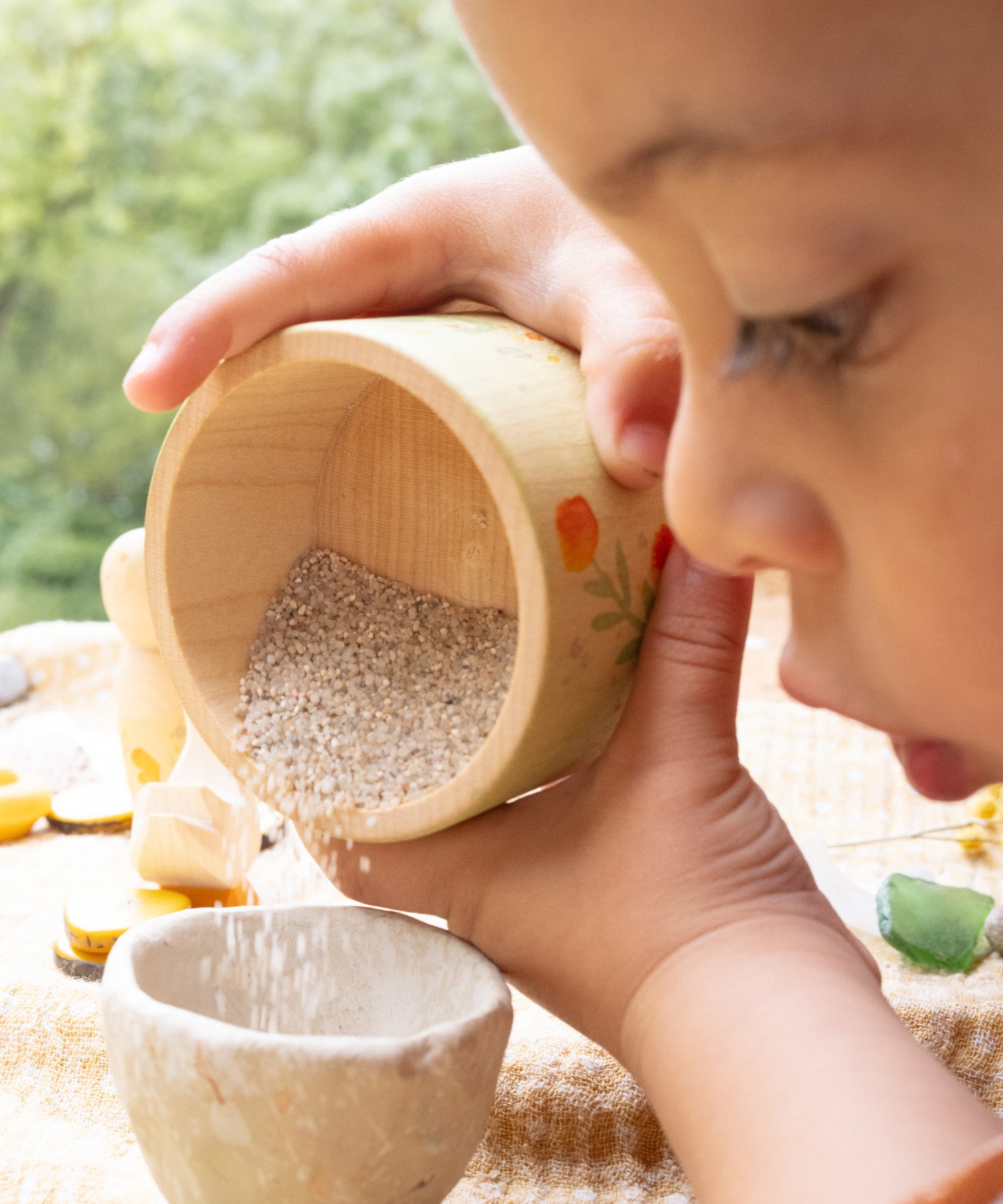 A child playing outside and holding the small wooden bowl from the Grapat / Ostheimer set showing the scale and tipping sand into a small stone bowl
