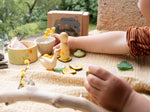 A child playing outside with the Grapat / Ostheimer Hello Summer set showing all 5 hand cut figures on a table cloth with the decorative cardboard box in the background. Bowl and peg doll has a delicate hand painted design