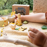 A child playing outside with the Grapat / Ostheimer Hello Summer set showing all 5 hand cut figures on a table cloth with the decorative cardboard box in the background. Bowl and peg doll has a delicate hand painted design