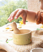 A child hand about to pick up the wooden peg doll standing in the small wooden bowl from the Grapat / Ostheimer Hello Summer set  showing the delicate hand painted detail and scale