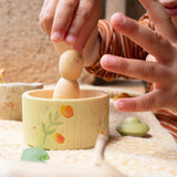 A child's hand picking up the wooden peg doll standing inside the small bowl from the Grapat / Ostheimer Hello Summer set showing the scale and delicate hand painted detail.
