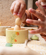 A child's hand picking up the wooden peg doll standing inside the small bowl from the Grapat / Ostheimer Hello Summer set showing the scale and delicate hand painted detail.