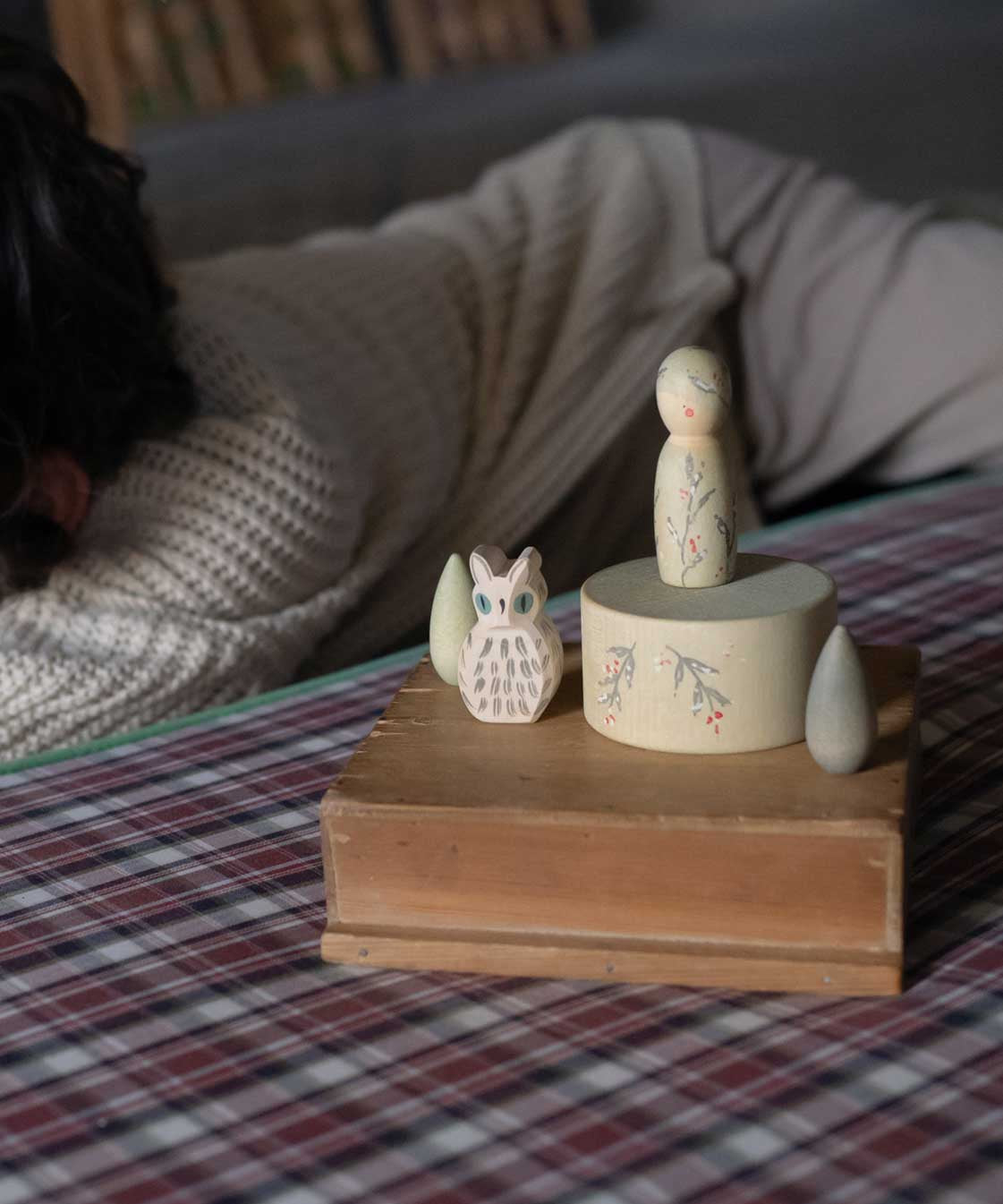 The Grapat Ostheimer Limited Edition Hello Winter wooden toy set available at Babipur. Features 5 hand cut and hand painted figures and pieces including a peg doll, small decorative bowl, owl and 2 green coloured snowdrop mandala pieces. The set has been placed on a wooden box, a child can be seen laying in the background. 