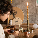 The Grapat Ostheimer Limited Edition Hello Winter wooden toy set available at Babipur. Features 5 hand cut and hand painted figures and pieces including a peg doll, small decorative bowl, owl and 2 green coloured snowdrop mandala pieces. The pieces from the set have been placed on a wooden surface and surrounded by bit of rocks and crystals. Two children are standing in front of them reaching for some of the pieces.