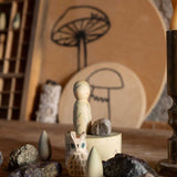 The Grapat Ostheimer Limited Edition Hello Winter wooden toy set available at Babipur. Features 5 hand cut and hand painted figures and pieces including a peg doll, small decorative bowl, owl and 2 green coloured snowdrop mandala pieces. The pieces from the set have been placed on a wooden surface and surrounded by bit of rocks and crystals. 