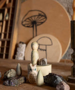 The Grapat Ostheimer Limited Edition Hello Winter wooden toy set available at Babipur. Features 5 hand cut and hand painted figures and pieces including a peg doll, small decorative bowl, owl and 2 green coloured snowdrop mandala pieces. The pieces from the set have been placed on a wooden surface and surrounded by bit of rocks and crystals. 