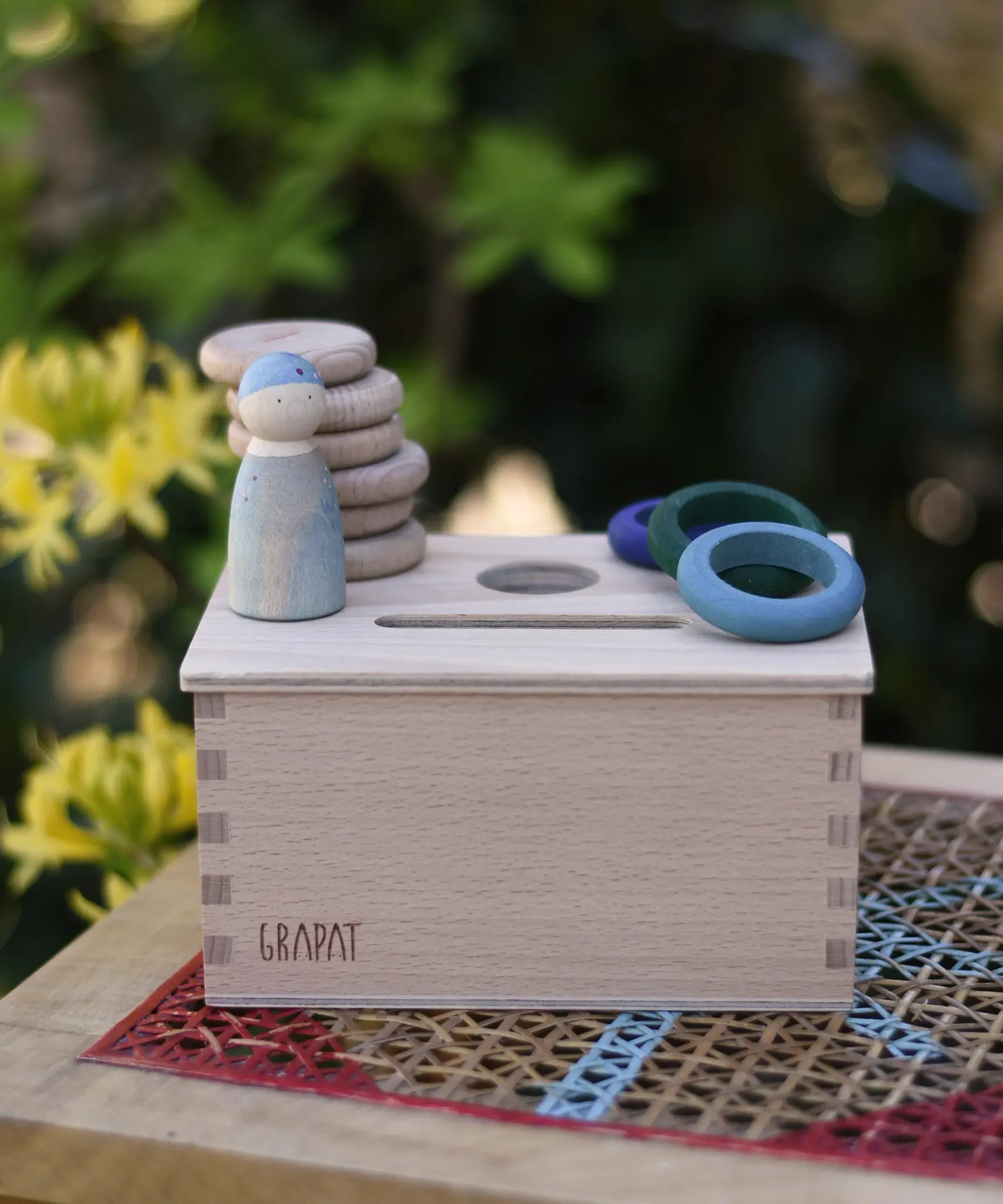 Grapat object permanence box with wooden coins, rings and Nins placed on the lid.