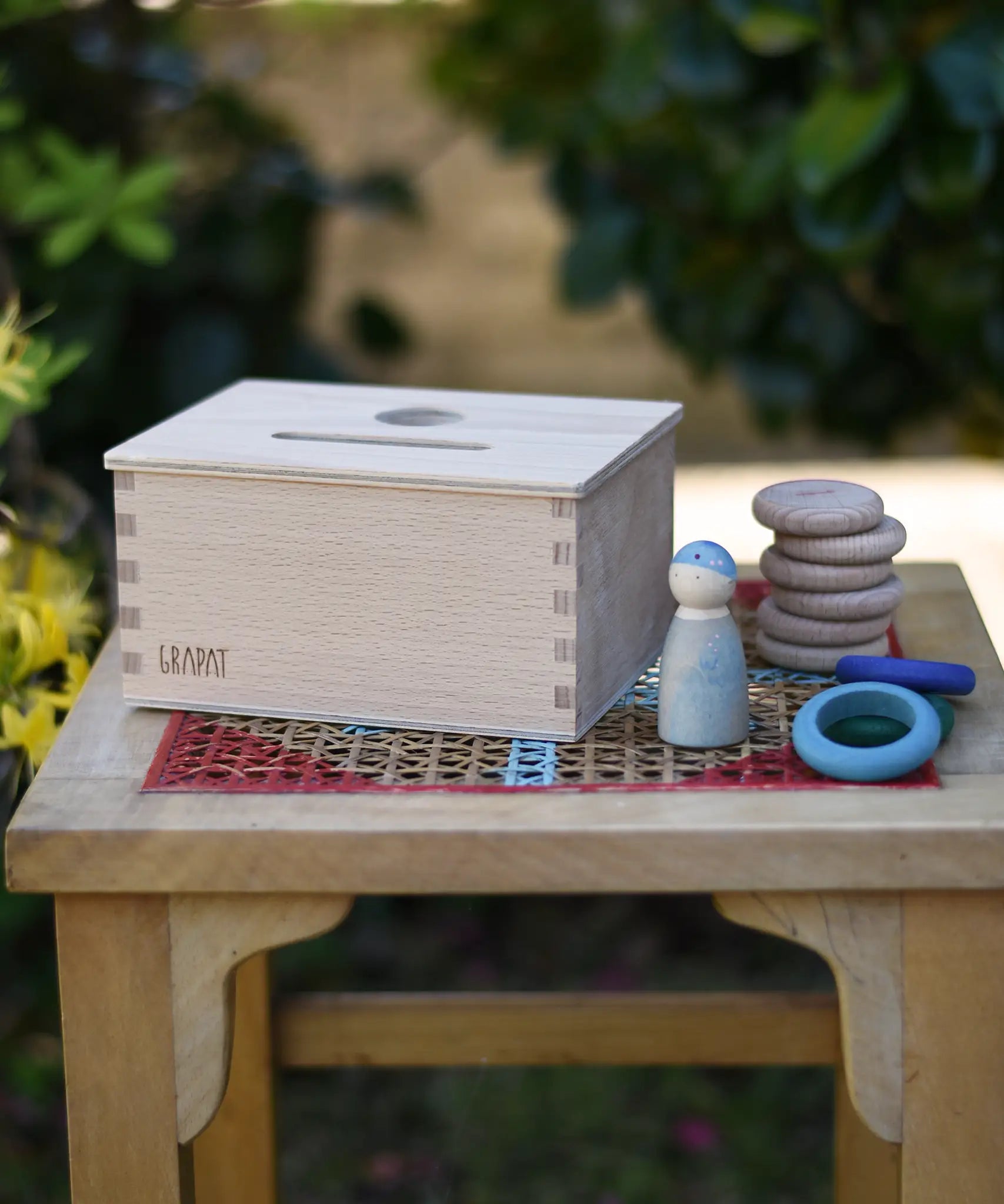 Grapat object permanence box placed on a stool with Nins, coins and rings placed besides it.