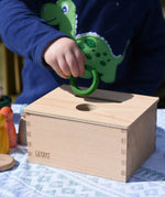 Child posting a green ring into the slot on the Grapat object permanence box. 