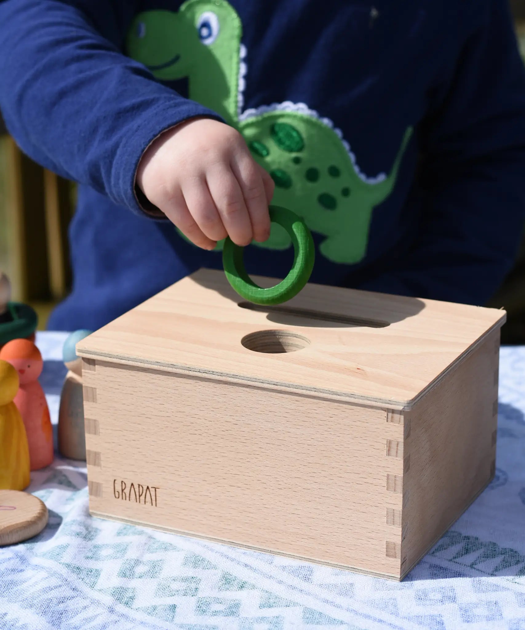 Child posting a green ring into the slot on the Grapat object permanence box. 