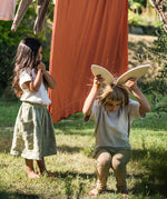 A child holding two of the Grapat petals wooden platforms above tjher head to look like bunny ears. These are a set of 24 wooden petals. These wooden petals are part of a huge range of open ended wooden toys from Grapat available here at Babipur.