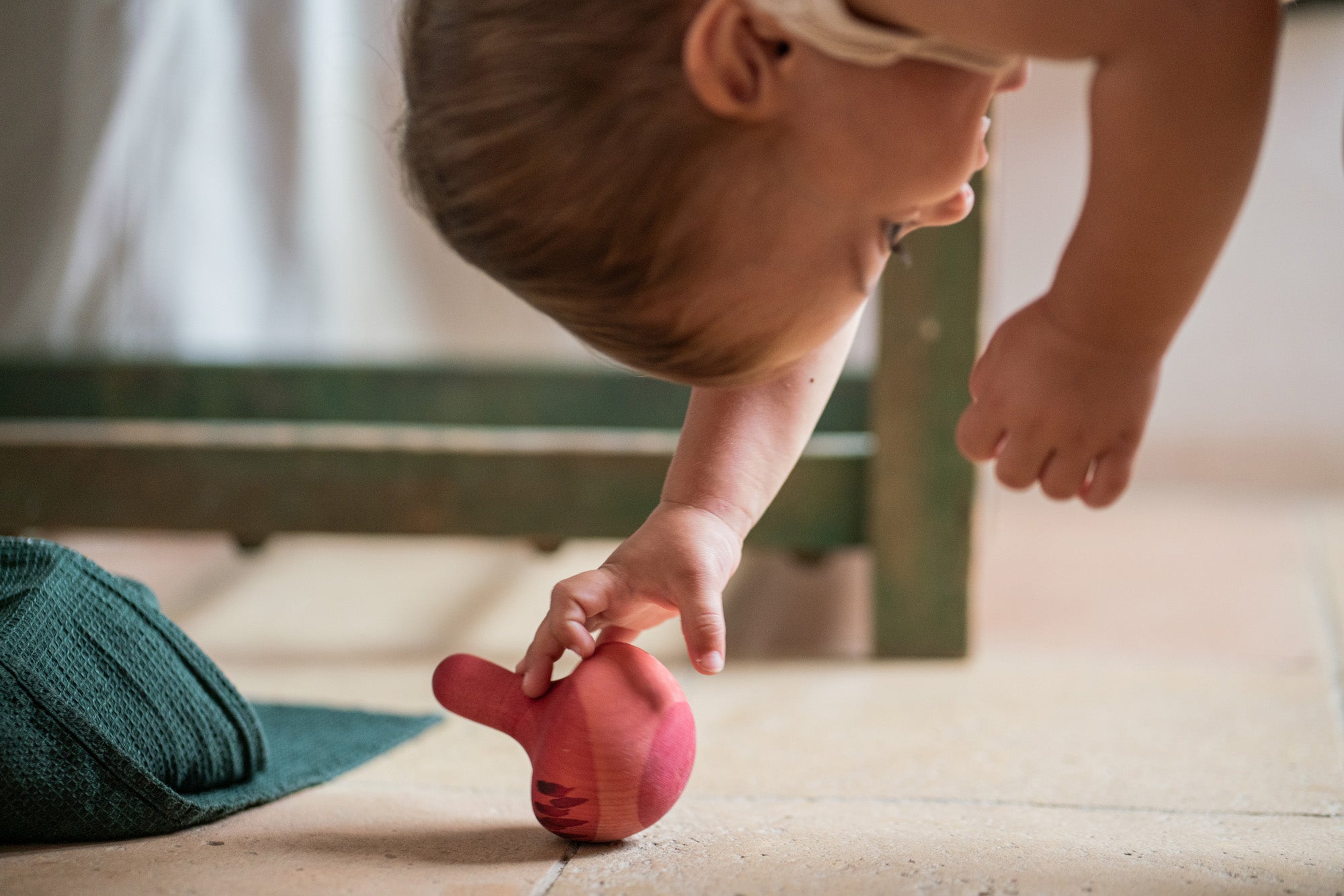 Child playing with the Grapat wooden pink chill wobbly bird on the stone floor showing the hand painted purple feather detailing.