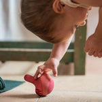 Child playing with the Grapat wooden pink chill wobbly bird on the stone floor showing the hand painted purple feather detailing.