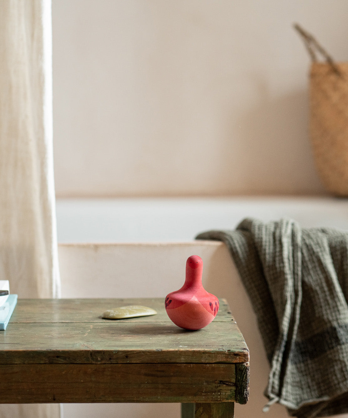 A close up of the Grapat wooden pink chill wobbly bird on a wooden table in the bathroom. Showing the hand painted pink face detail