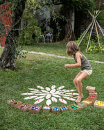 Young girl playing with grapat mandala pieces and the wooden petal platforms on some grass