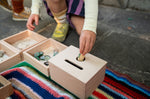 Close up of child's hand putting a Grapat nin inside the Grapat wooden permanence box on a striped blanket