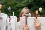 Child standing behind a washing line with clothes hanging. Different Grapat handcrafted wooden puppets played with showing the different faces. Features the light grey owl, dark grey wolf, purple fairy and light green little boy wooden puppet. 