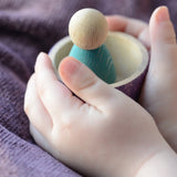 A child holding a Grapat handcrafted wooden sorting bowl with a peg doll standing inside