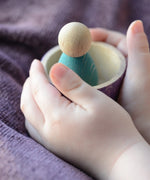A child holding a Grapat handcrafted wooden sorting bowl with a peg doll standing inside