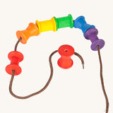 Grapat Wooden rainbow coloured Spools shown threaded onto a lace. These wooden toys are part of a wide range of open ended toys available at Babipur.  