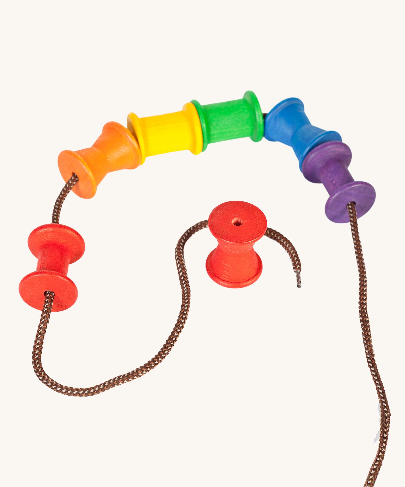 Grapat Wooden rainbow coloured Spools shown threaded onto a lace. These wooden toys are part of a wide range of open ended toys available at Babipur.  