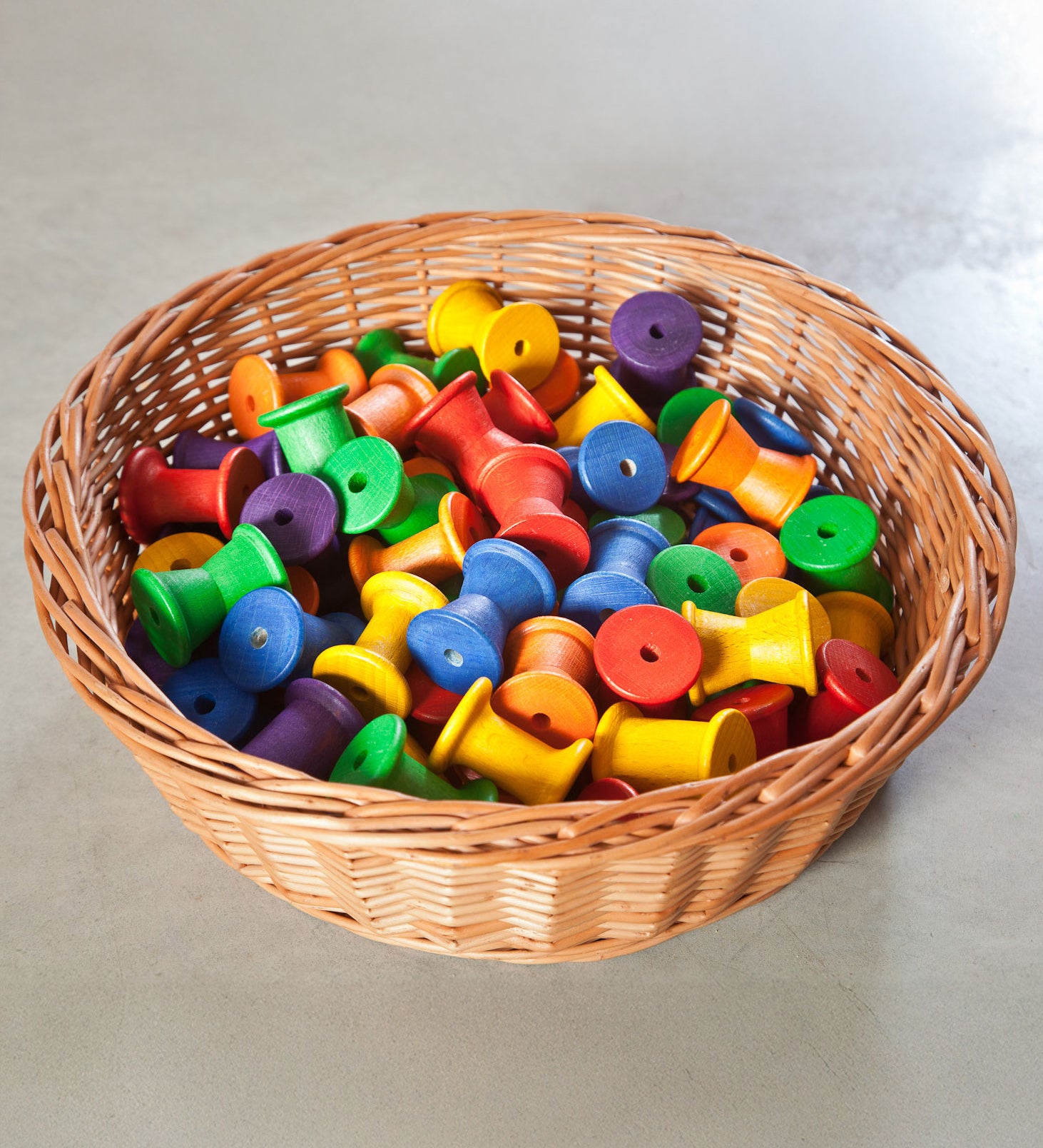 Grapat 36 Wooden Spools shown placed in a wicker basket. These wooden toys are part of a wide range of open ended toys available at Babipur.  