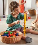A child playing with the Grapat set of 36 wooden rainbow coloured spools, stacking the yellow spool on top of each other. These wooden toys are part of a wide range of open ended toys available at Babipur.  